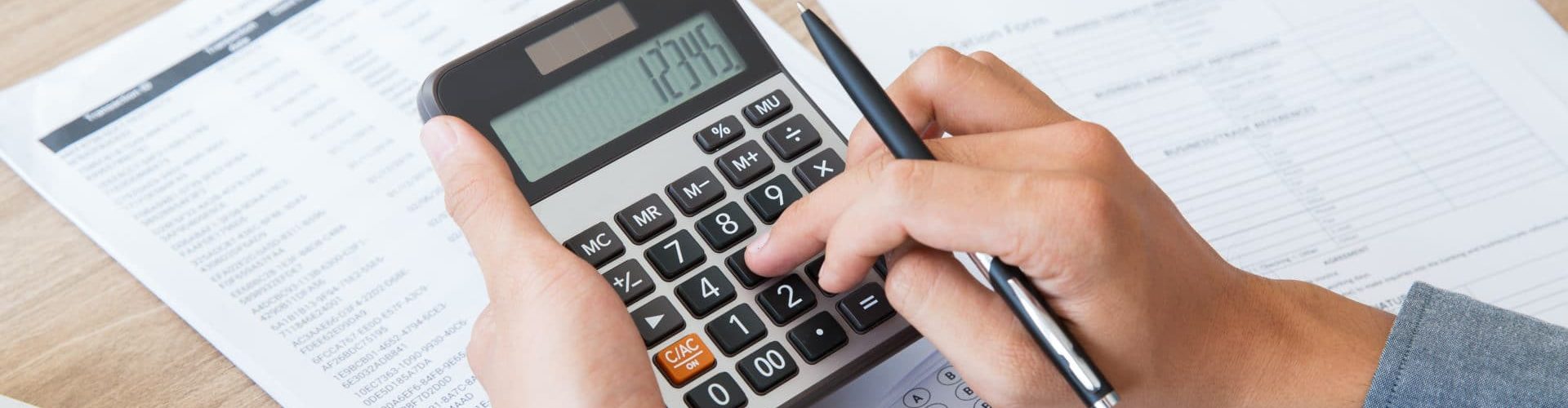 Unrecognizable businessman using calculator to find out income and outcome. He counting company finances. Male hands with pen pushing button at desk. Investment or paperwork concept