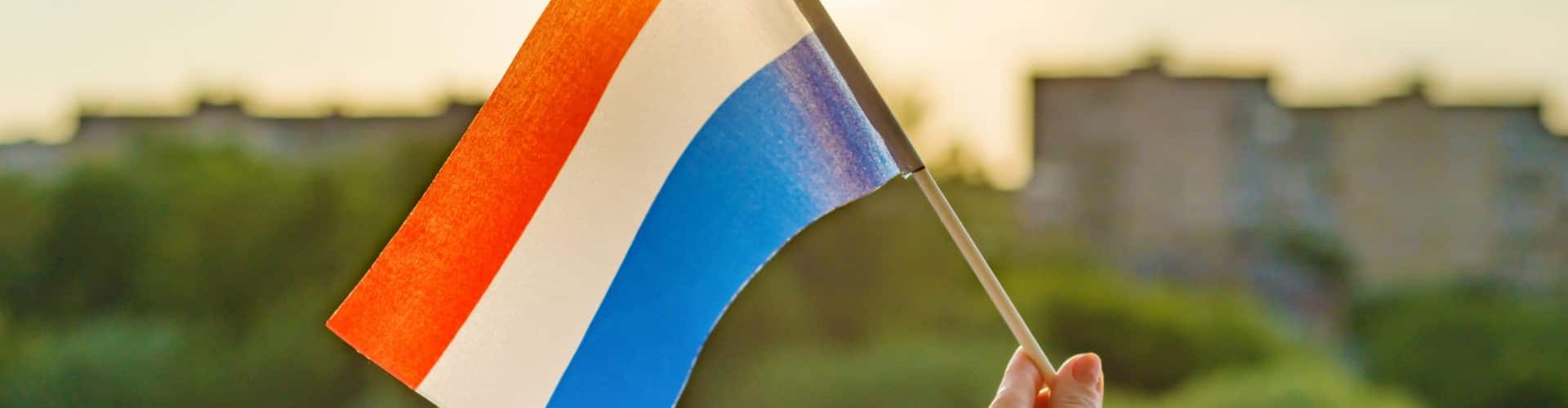 Hand holds Netherlands flag an open window
