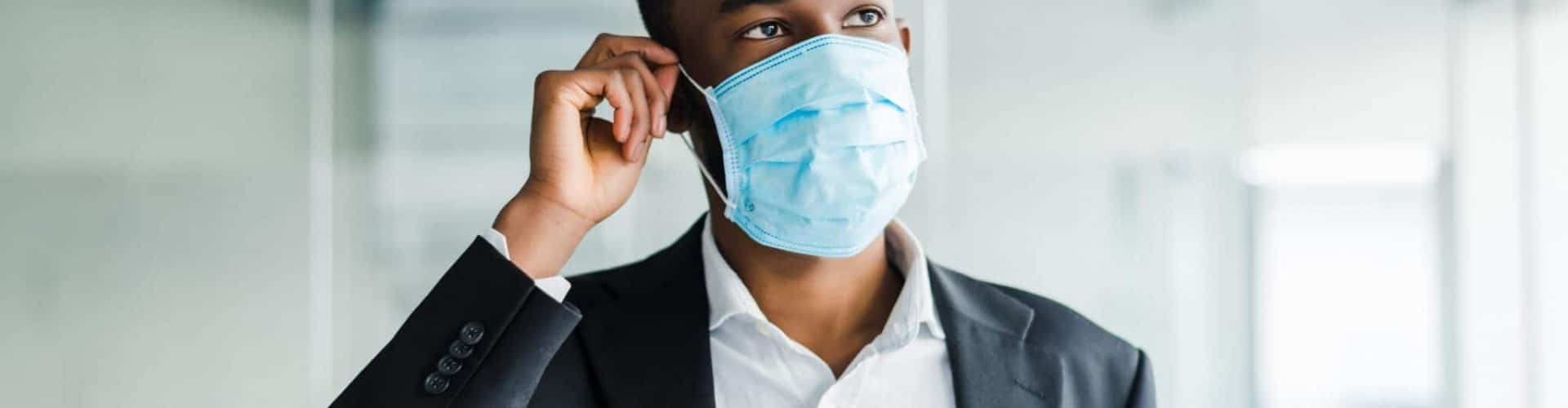 African young business man wearing a mouth protection to prevent getting sick at work in office